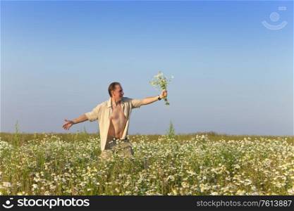 The happy young man in the field with a bouquet of camomiles