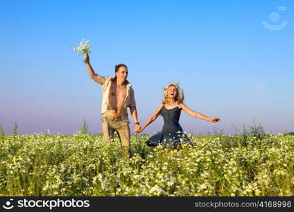 The happy young pair in the field of chamomiles jumps