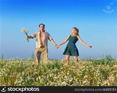 The happy young pair in the field of chamomiles jumps