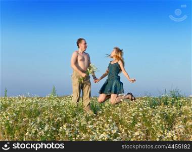The happy young pair in the field of chamomiles jumps