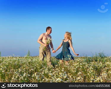 The happy young pair in the field of chamomiles jumps