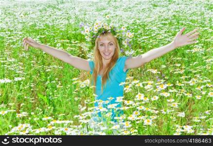 The happy young woman in a wreath from wild flowers in the field