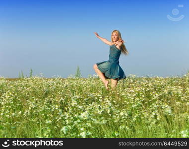 The happy young woman jumps in the field of camomiles