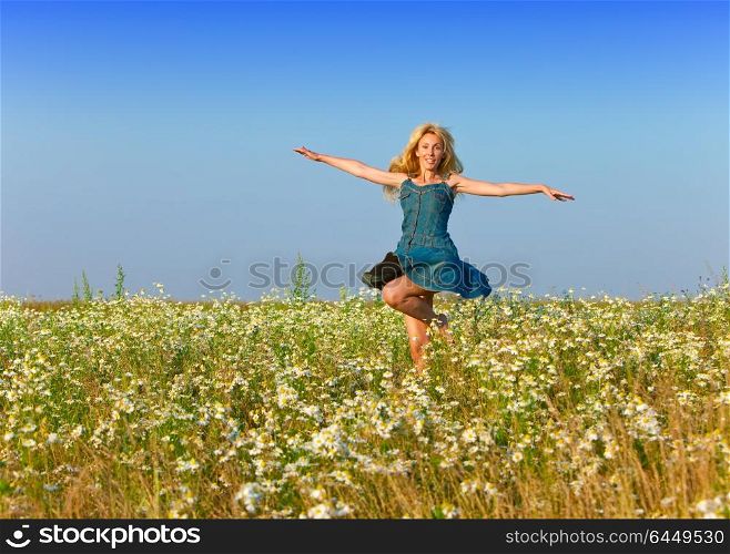 The happy young woman jumps in the field of camomiles