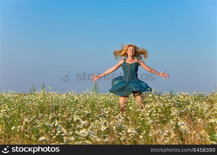 The happy young woman jumps in the field of camomiles