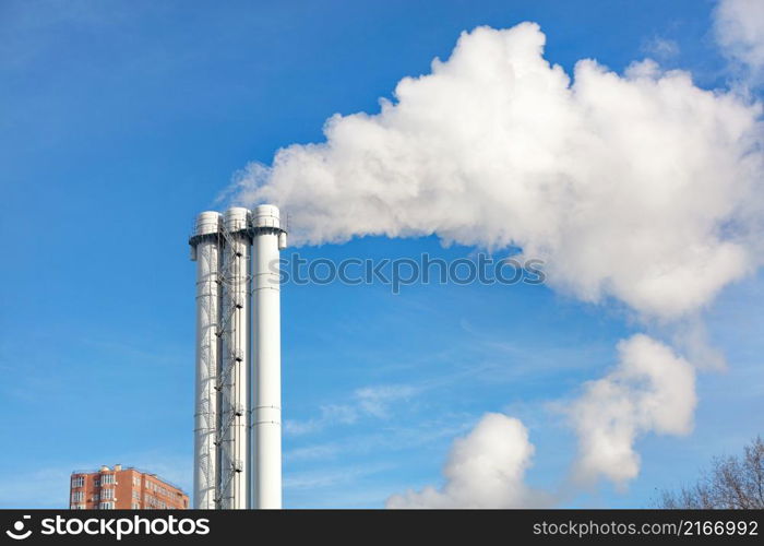 The high triple white chimney of the CHP plant emits smoke and steam into the atmosphere. The concept of preserving the atmosphere and the environment from pollution and emissions. ?opy space.. Emissions of smoke and steam from a CHP chimney in a clear sky.