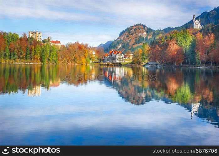 The Hohenschwangau resort, with the Neuschwanstein and Hohenschwangau castles, surrounded by autumn forests and reflected in the Alpsee lake water.