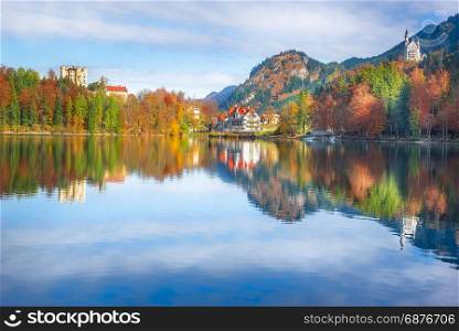 The Hohenschwangau resort, with the Neuschwanstein and Hohenschwangau castles, surrounded by autumn forests and reflected in the Alpsee lake water.