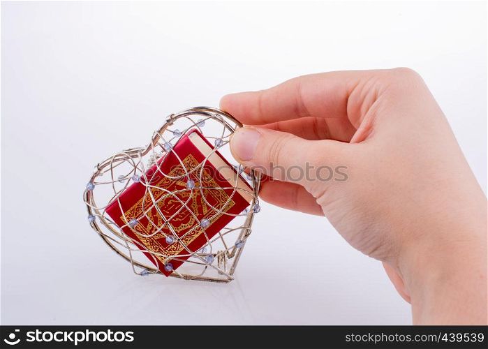 The Holy Quran in a heart shaped cage on a white background