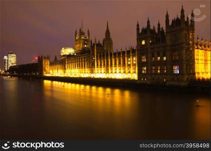 The Houses of Parliament lit up at night, bright yellow lights reflecting on the River Thames