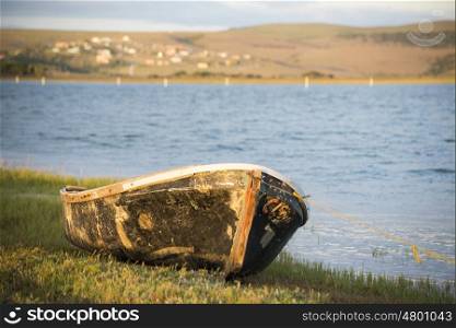 The hull of an old boat lies on the bank of the river.