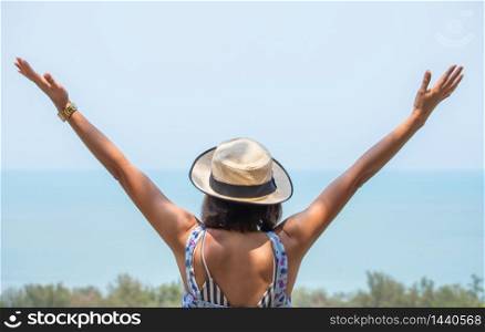 The image behind Asian women raise their arms and wear a hat background sea.