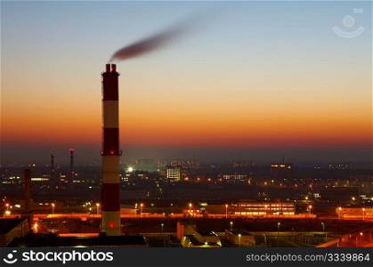 The image of a smoking factory pipe against a sunset