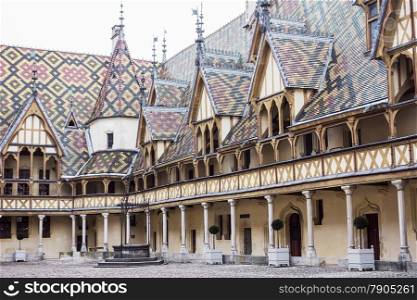 The inner courtyard at the Hospices de Beaune features a well and an ornate decorated roof with patterns made from yellow, red and green tiles.