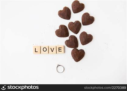 The inscription in wooden letters love, small truffle candies in the form of a heart. Ring with a diamond - a proposal of a hand and a heart. The inscription in wooden letters love, small truffle candies in the form of a heart. Ring with a diamond - a proposal of a hand and a heart.