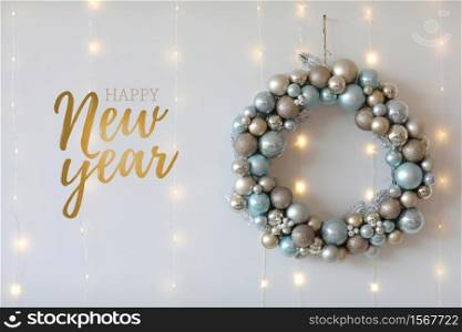 The inscription of Happy New Year, wreath of Christmas balls on a white wall and lights background. New Year&rsquo;s card, festive background. The inscription of Happy New Year, wreath of Christmas balls on a white wall and lights background. New Year&rsquo;s card, festive background.