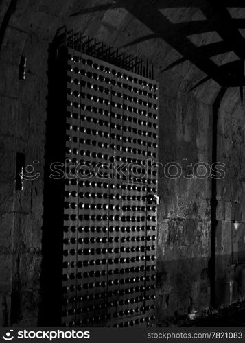 The inside castle gate to Edinburgh Castle at night shows a little bit of light reflecting off the metal studs in the door and shadows from the portcullis. In black and white.