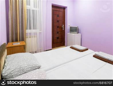 The interior of a small room with a double bed, a window, a TV and a fridge