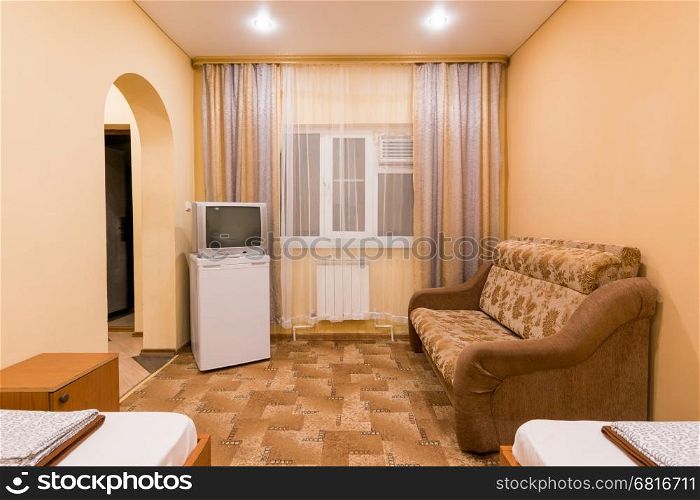 The interior of a small room with sofa bed and two single beds, window, TV and fridge