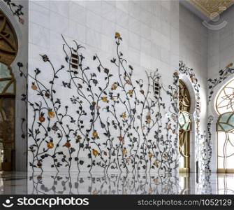 The interior walls decorated with intricate floral inlays of the Sheikh Zayed Grand Mosque in Abu Dhabi, UAE