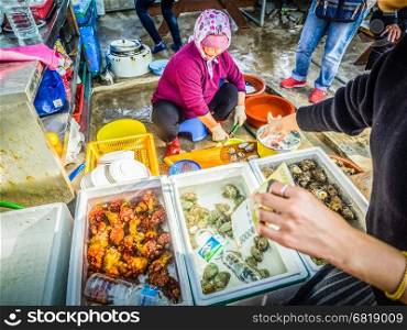 The Jeju woman prepare raw seafood to serve to her customer in seafood shop near Seongaksan mountain, Jeju island, South Korea.