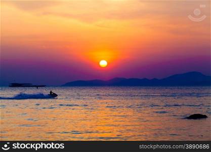 the jetski above the water at sunset. Silhouette of people on a jet ski running pass the romantic sunset in the sea.