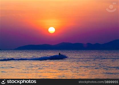 the jetski above the water at sunset. Silhouette of people on a jet ski running pass the romantic sunset in the sea.