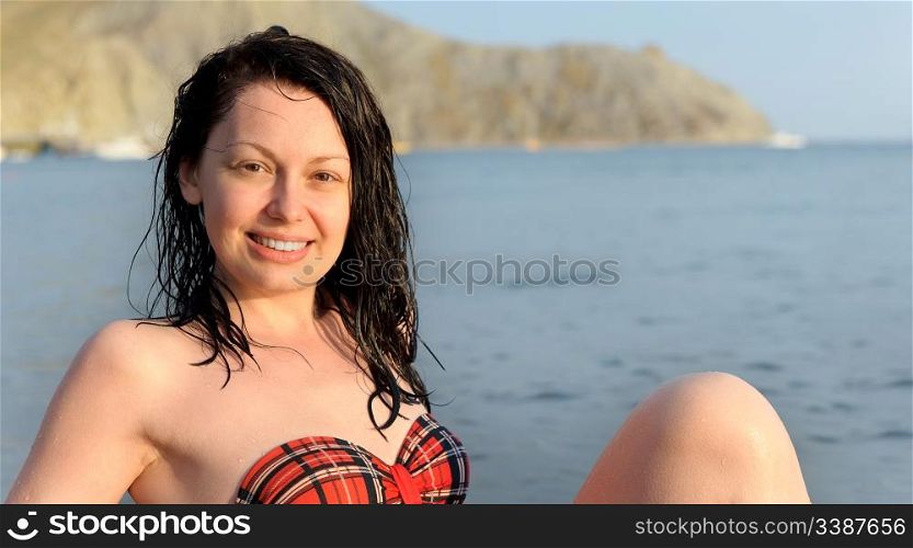 The joyful woman sits on sea coast