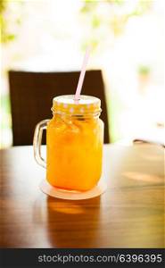The jur cup full of fresh orange juice with cocktail straw on wooden table. Fresh orange pleasure
