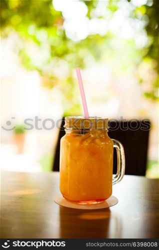 The jur cup full of fresh orange juice with cocktail straw on wooden table. Fresh orange pleasure