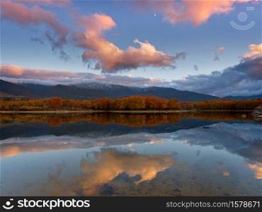 The lake in autumn at dusk with landscape reflections and clouds