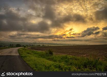 The landscape at the road through in the field with colorful clouds