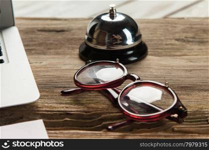The laptop, blank paper, glasses and small bell on the wooden table. concept of workplace