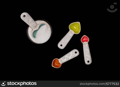 The largest of the heart shaped spoons is in the round bowl of sugar, while the others are facing in other directions on the isolated black backround.