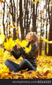 The laughing girl throws autumn leaves in park. Seasons
