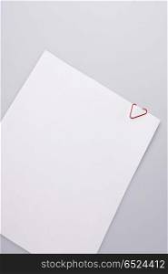 The laying empty leaf of a paper is clamped by a paper clip in the form of heart. Leaf of paper with heart
