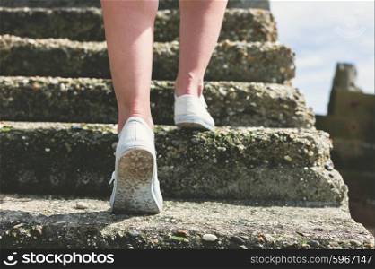 The legs and feet of a young wmoan as she is walking up some step by the sea