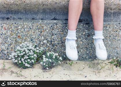 The legs and feet of a young woman as she is sitting on a wall by the sea