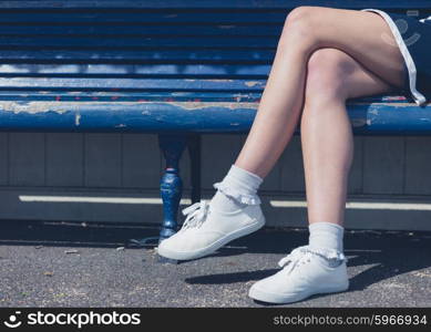 The legs and feet of a young woman sitting on a bench on a sunny day in summer