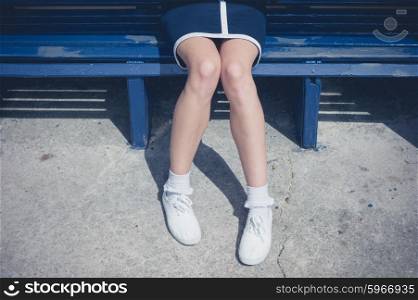 The legs and feet of a young woman sitting on a bench on a sunny day in summer