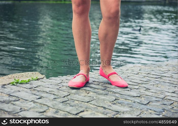 The legs and feet of a young woman standing by a canal