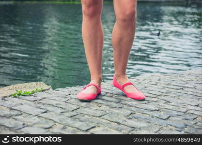 The legs and feet of a young woman standing by a canal