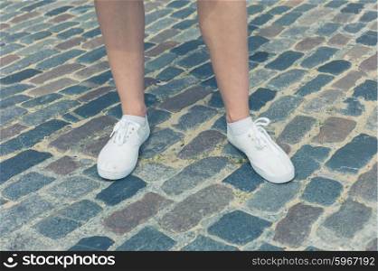 The legs and feet of a young woman standing on a cobbled stret