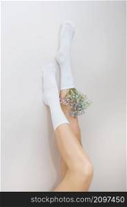 The legs of a girl in white socks in which there are flowers stand up. The concept of smooth and beautiful legs. The legs of a girl in white socks in which there are flowers stand up. The concept of smooth and beautiful legs.
