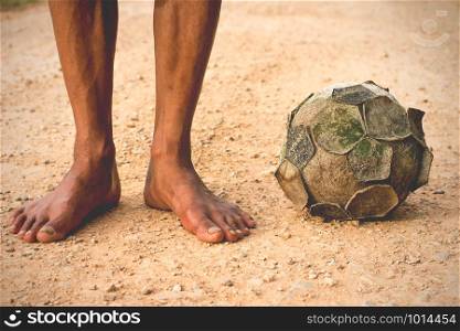 The legs of a man standing with a soccer ball on a dirt old, vintage tone.