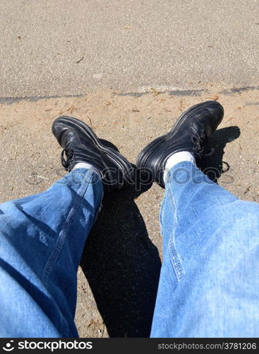The legs of a tired hiker sitting on a bench, resting from his walk.