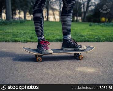 The legs of a trendy young person skteboarding on the concrete in a park