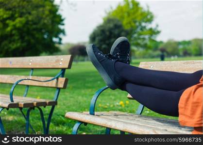 The legs of a young woman as she is lying on a bench in the park relaxing