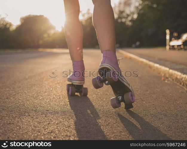 The legs of a young woman as she is roller skating in a park at sunset