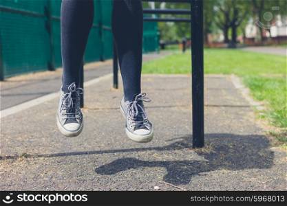 the legs of a young woman as she is sitting on a rail in a park on a summer day